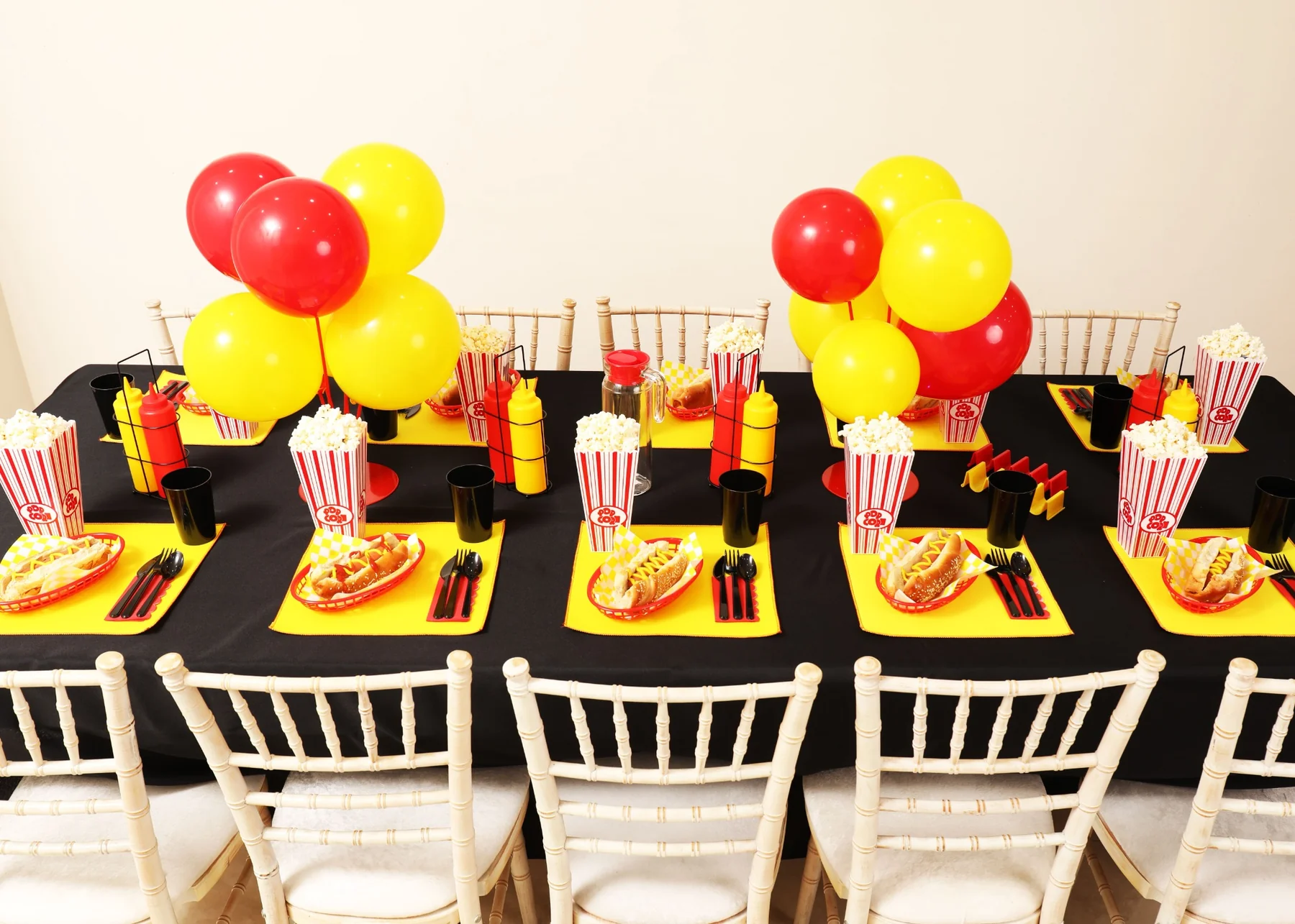 Bold cinema-themed party table with red and yellow balloons, popcorn and hot dogs